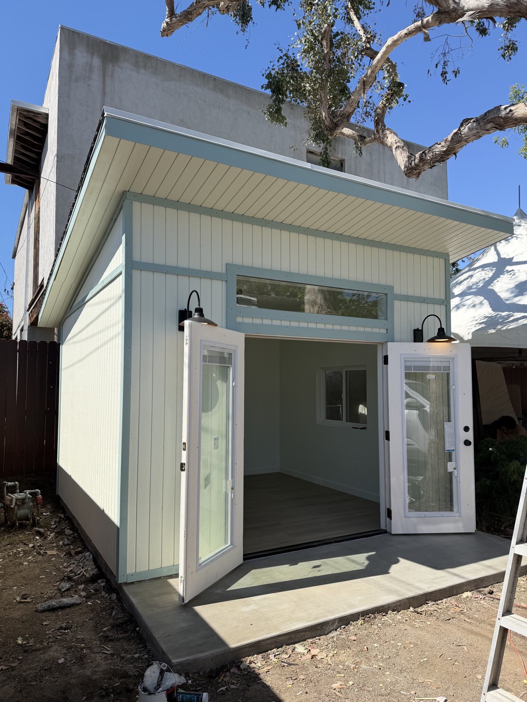 Sage green 12 by 12 ft yoga studio with double french doors open onto a concrete patio